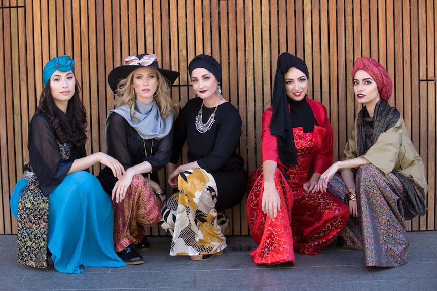 Five models wearing modest fashions crouched down in a line.