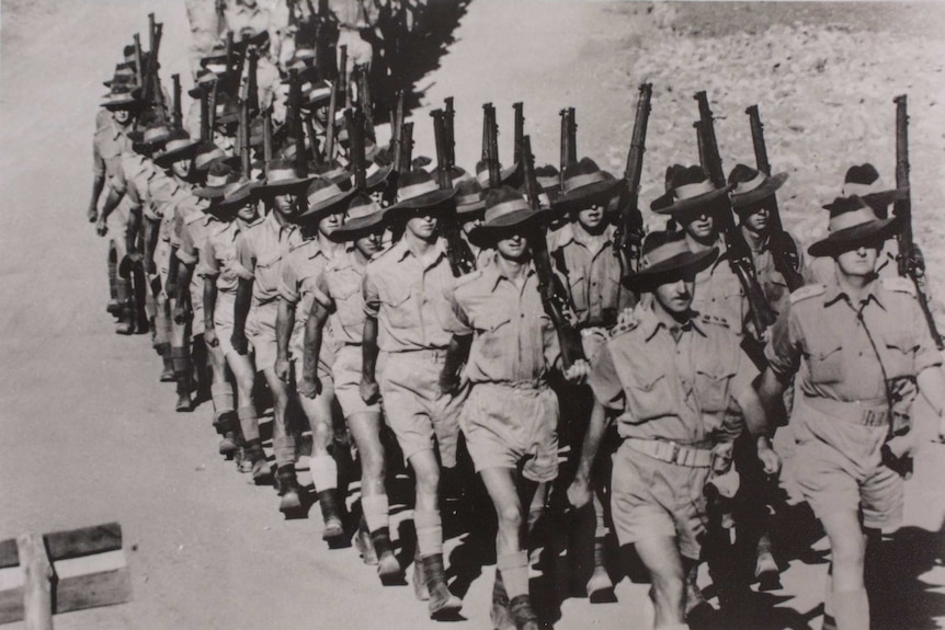 A black-and-white photo of a platoon of soldiers marches through Alice Springs carrying rifles.
