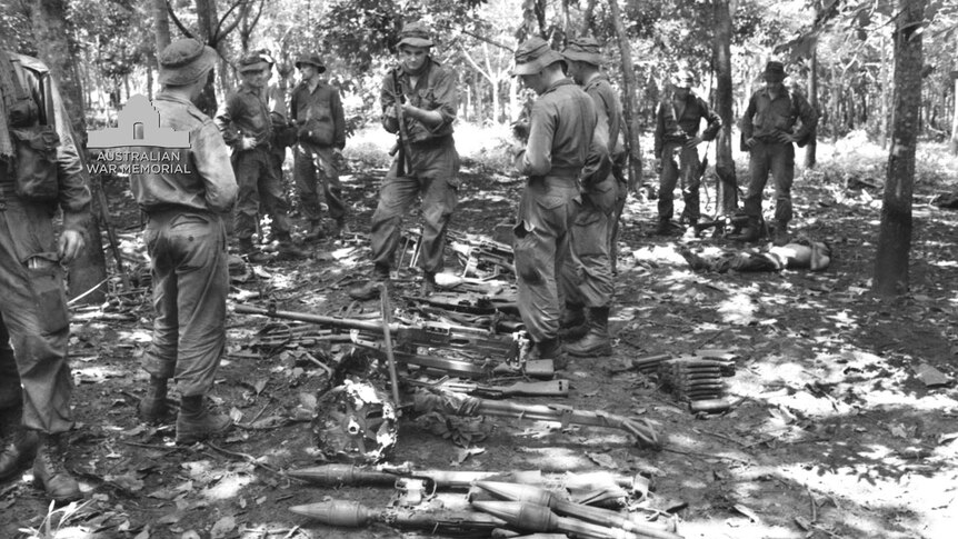 Troops in a clearing in the rubber plantation examine some of the Viet Cong weapons captured after the Long Tan battle.