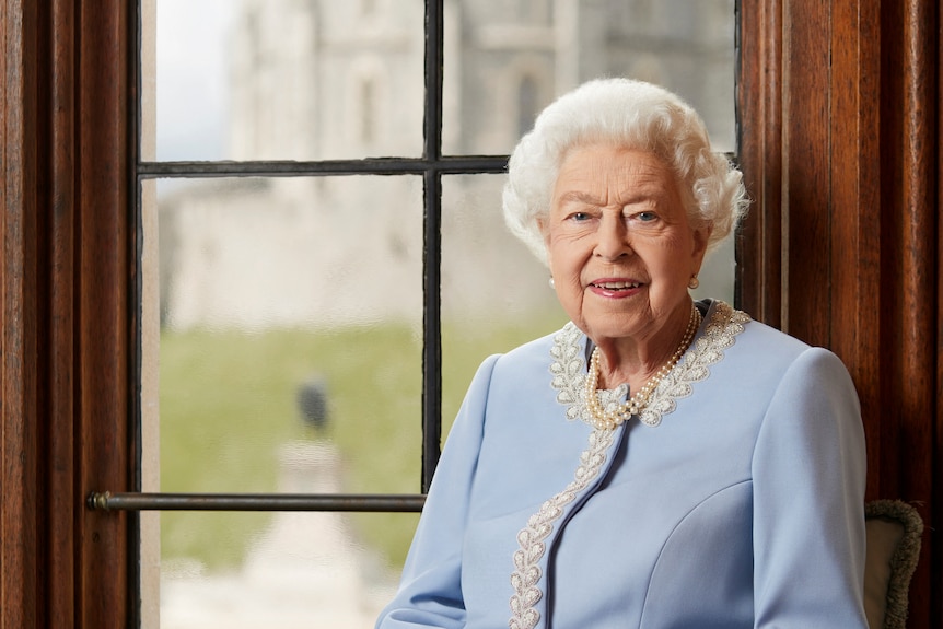 Queen Elizabeth II is pictured in front of a window wearing a blue outfit at Windor Castle. 