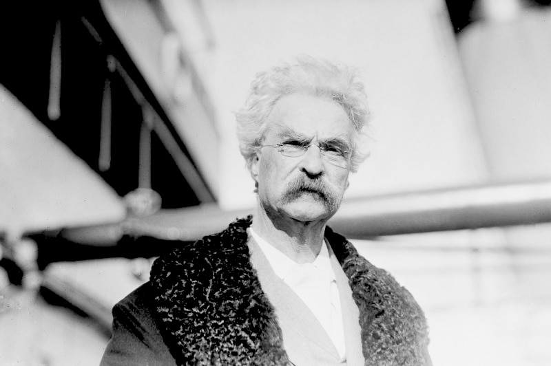 Black and white image of Mark Twain, with a a thick moustache and wearing a large coat.