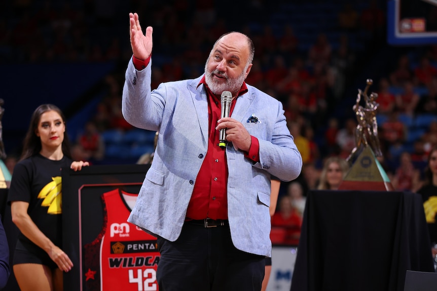 A man points to the sky while talking on a microphone.