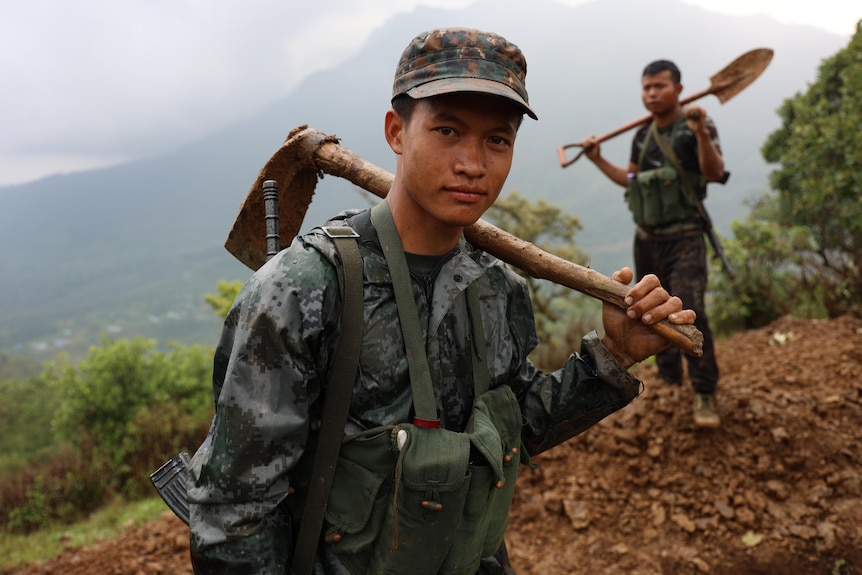Soldier looks at camera holding a tool in mud. 