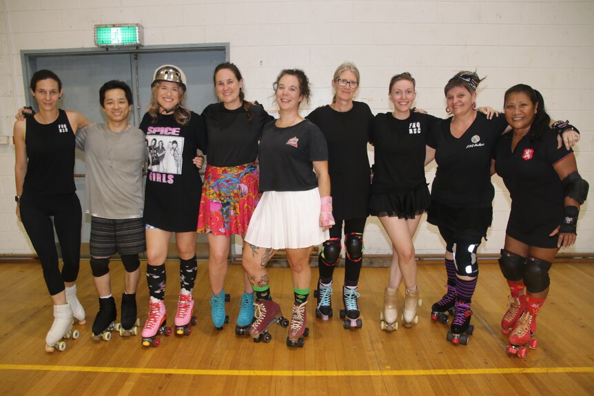 Nine adult females standing side by side on their roller skates 