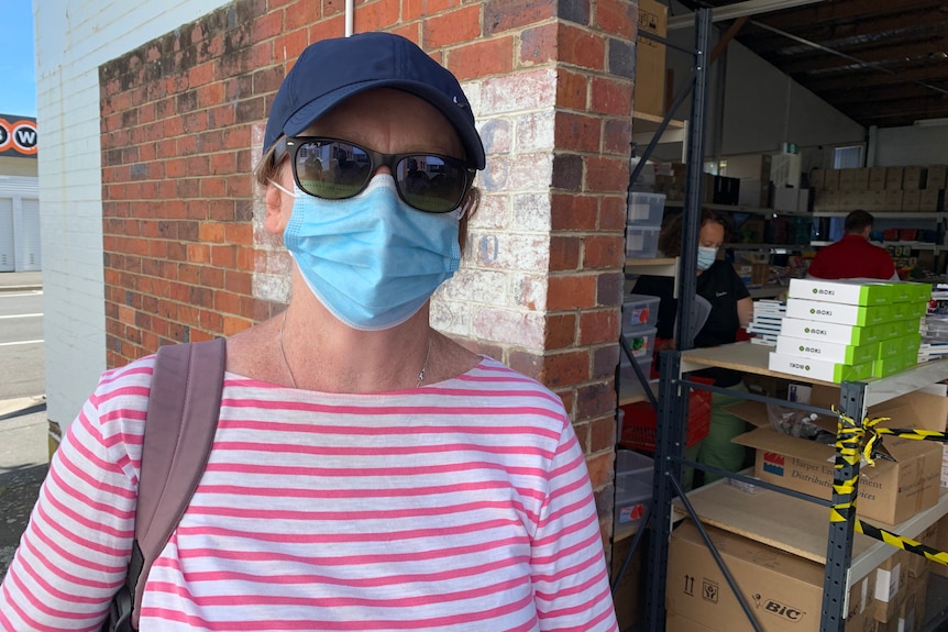 A woman wearing a cap and face mask outside a warehouse.