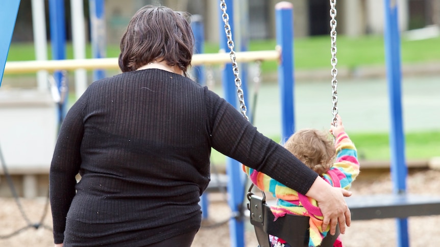 A woman and a child at a playground, the woman pushing a swing.