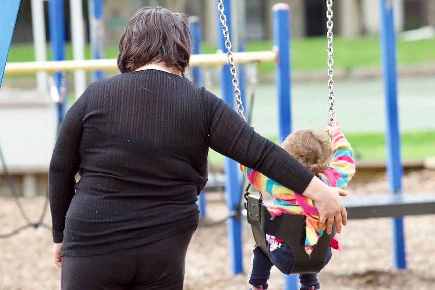 A woman and a child at a playground, with a fence obscuring the view.