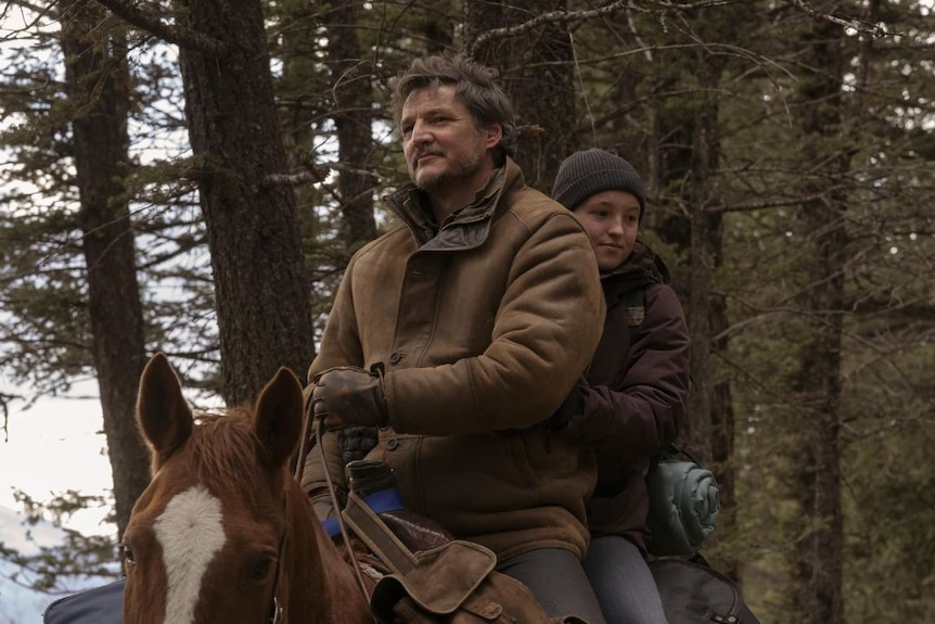 A man and a woman ride a brown horse through trees.