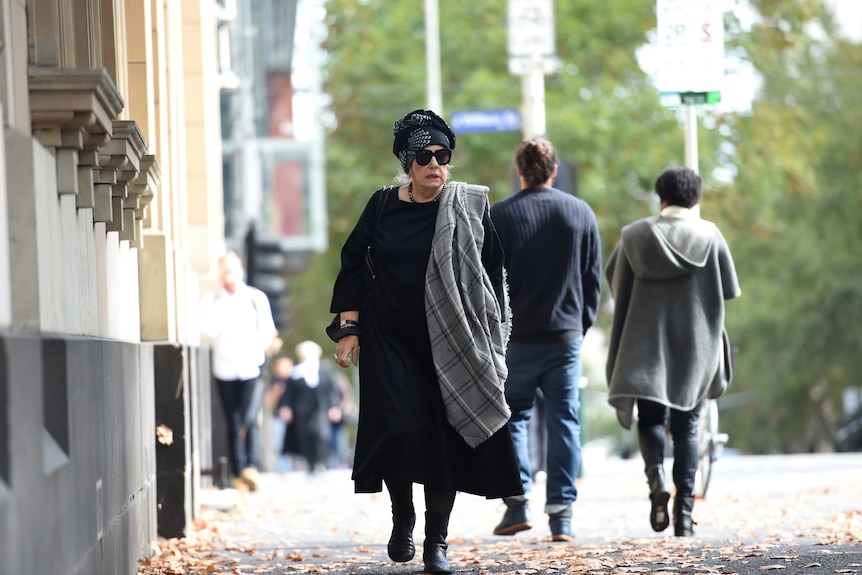 Wendy Whiteley, wearing a grey scarf over her shoulder and black sungalsses and a black head scarf