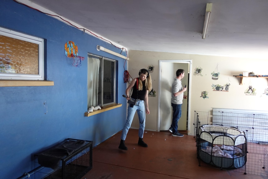 Woman holding audio equipment in a house standing next to a man in a doorway into another room.