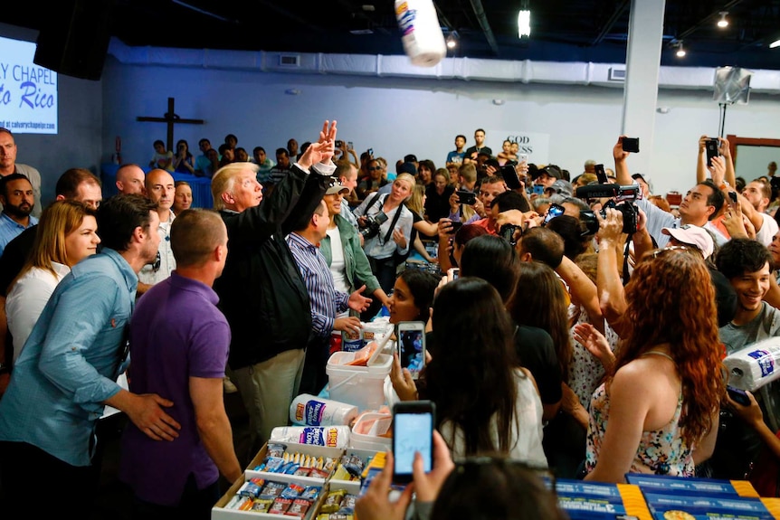 Donald Trump throws paper towel rolls into a crowd of people.