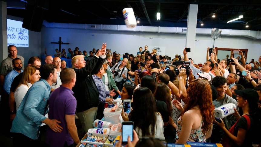 Donald Trump throws paper towel rolls into a crowd of people.