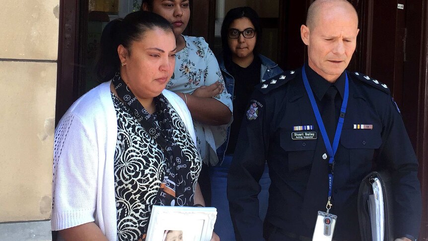 Zahraa Sahib outside court holding a photo of her niece Sanaya Sahib with other family members and a police officer.