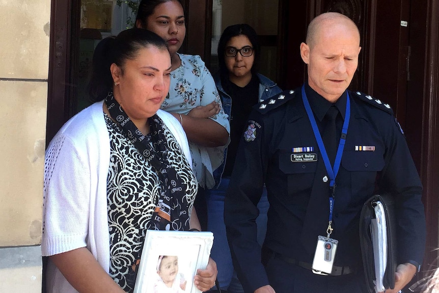 Zahraa Sahib outside court holding a photo of her niece Sanaya Sahib with other family members and a police officer.