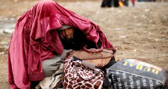 A displaced woman covers her daughter with a pink blanket, surrounded by their few belongings.