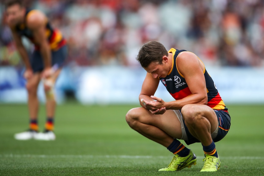An Adelaide Crows AFL player crouches as he looks down at the ground after a loss.