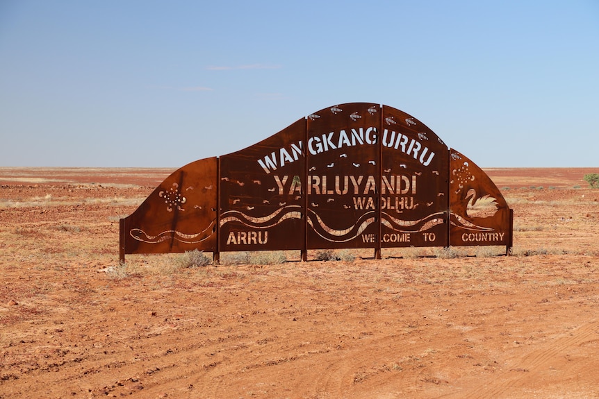 A brass metal sign, approximately 1 metre high and two meters long with the words 'Welcome to Wangkangurru Yarluyandi Country'