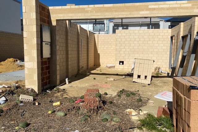 The messy-looking and overgrown surrounds of an unfinished brick home