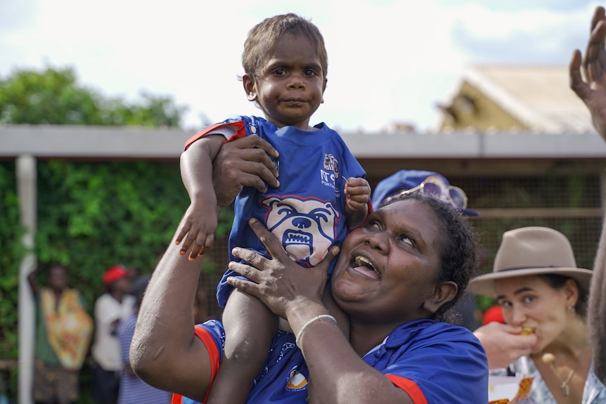 A young Walama Bulldogs fan is being help up on the shoulder of an adult at the Tiwi Islands football grand final.