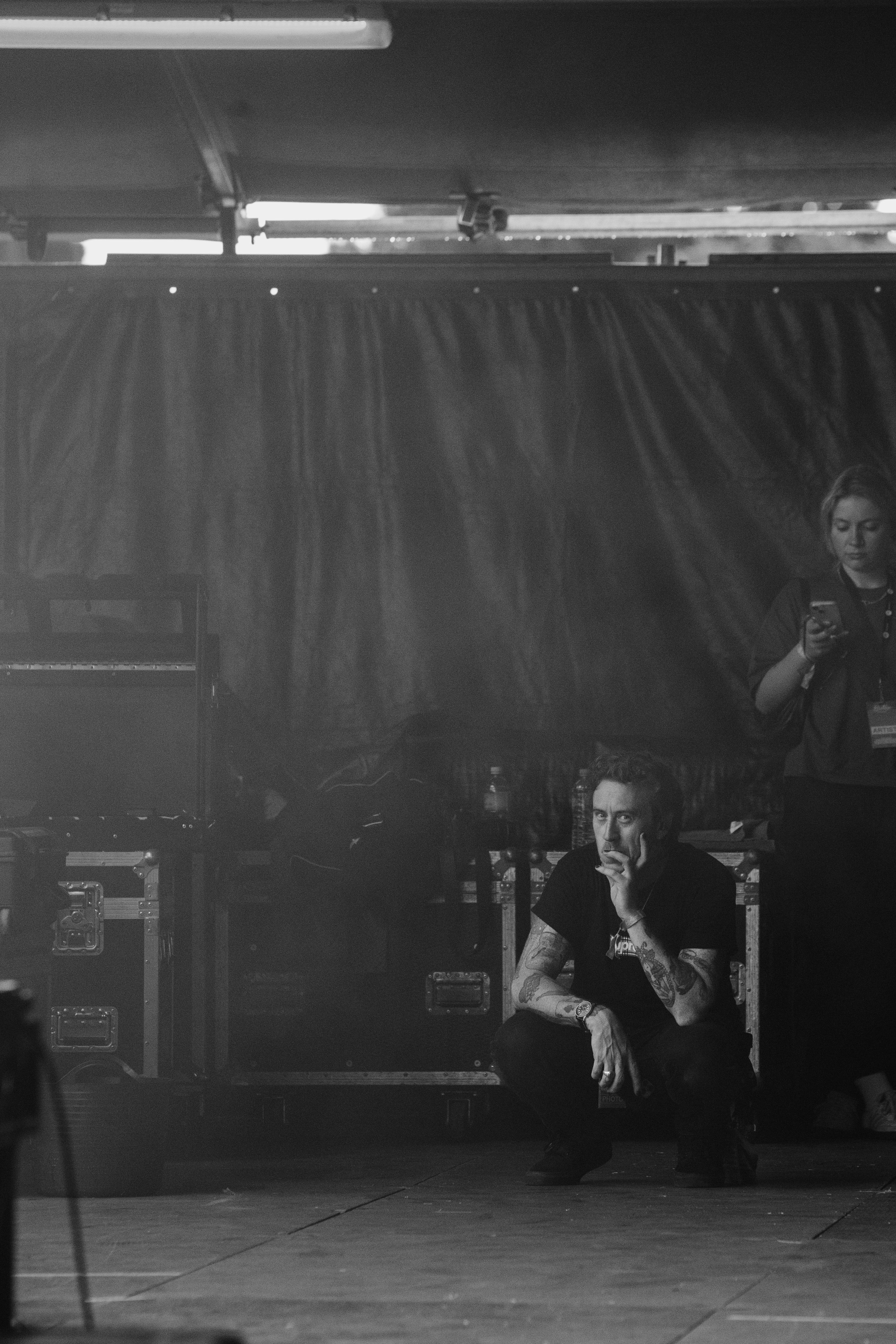 A man kneels down with his chin in one hand on the side of a stage