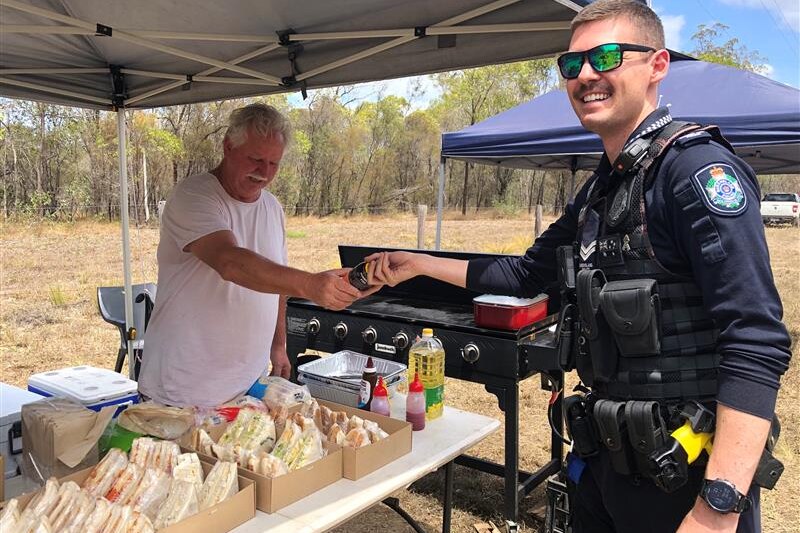 A man hands a sports drink to a police officer over a table filled with sandwiches