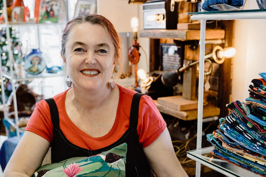 smiling woman in shop looking at lens holding cushions.