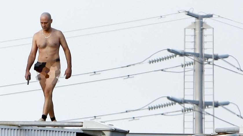 A naked man armed with a gun walks along the top of a billboard in the centre of Perth