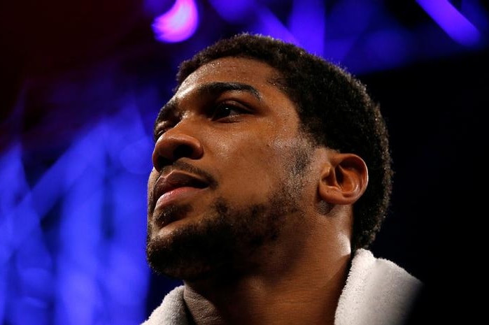 Anthony Joshua looks to the right as he stands with a towel around his neck, sweat beading on his forehead.