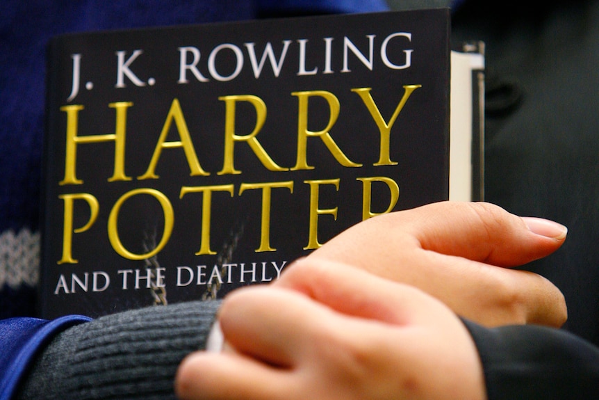 A child holds a copy of Harry Potter and the Deathly Hallows.