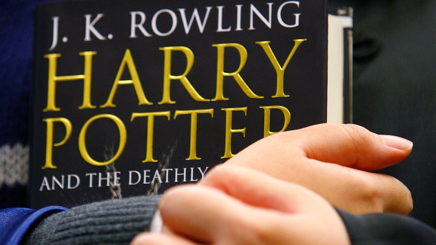 A child holds a copy of Harry Potter and the Deathly Hallows.