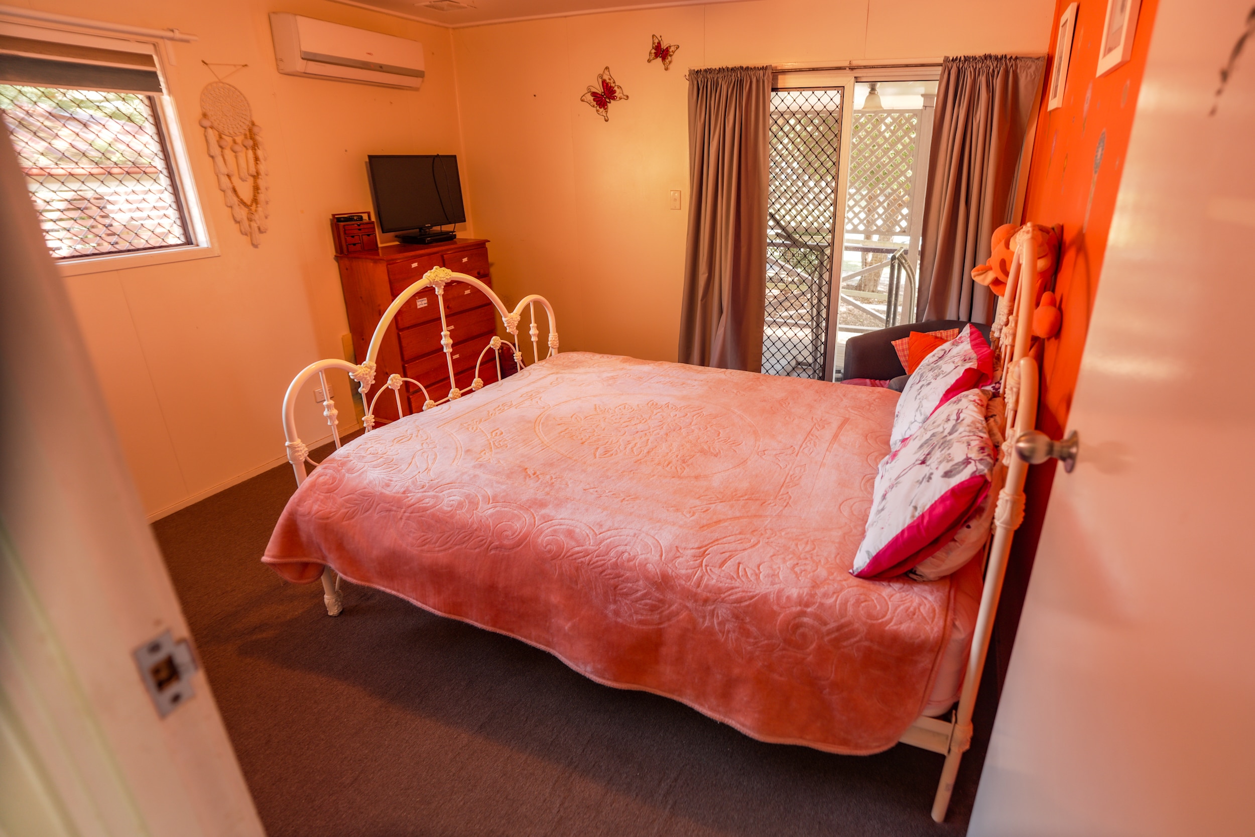 A bed with a pink quilt in a bedroom with an orange wall.