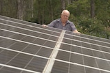 Alex Smith stands on a ladder with his hands on solar panels.
