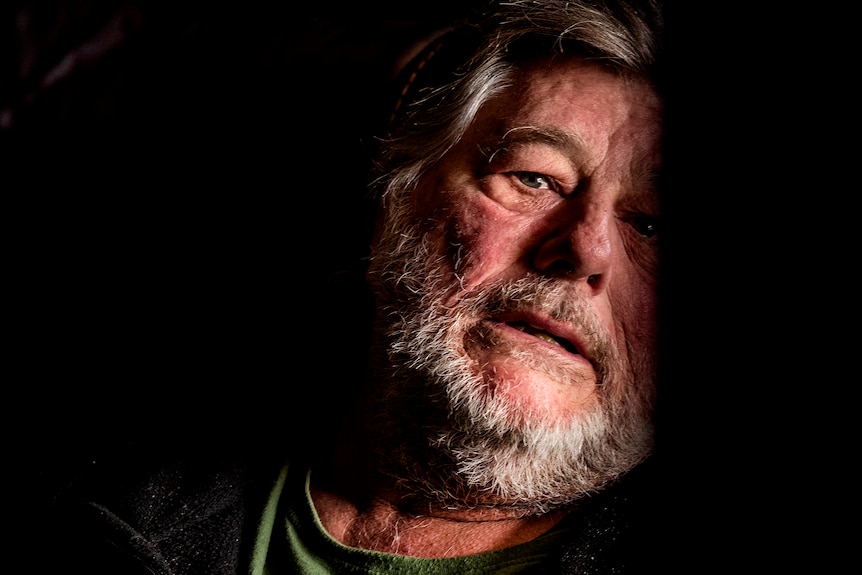 A bearded man in a darkened room.