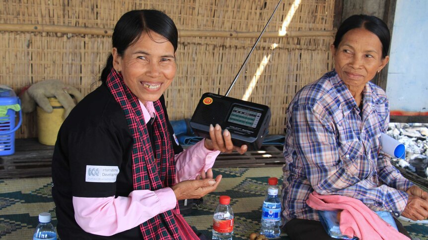 two women sitting on a mat holding a radio and smiling