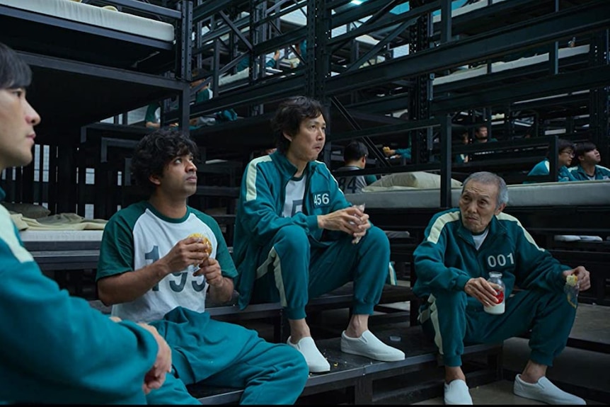 Four men wearing green tracksuits sitting and eating lunch 