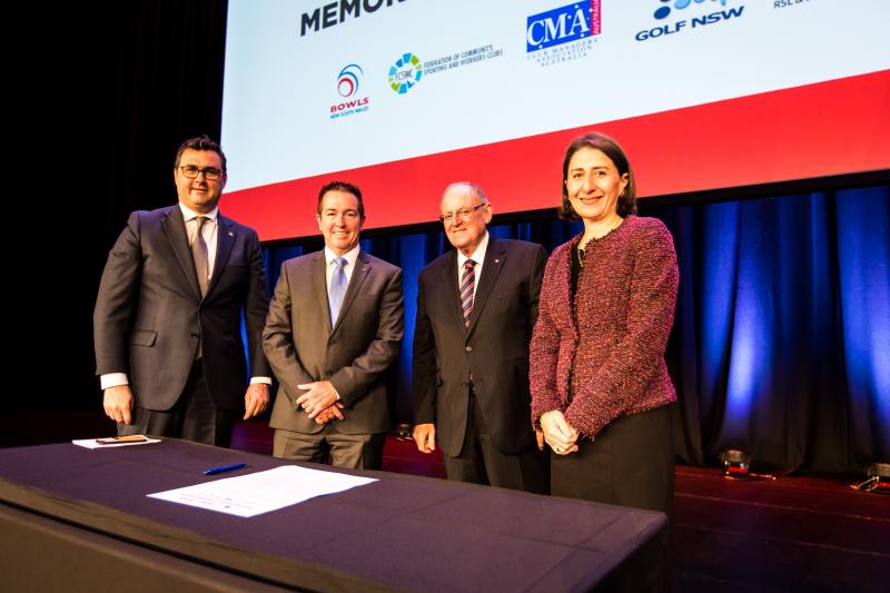 Three men and Premier Gladys Berejiklian stand behind a table, smiling. A large piece of paper is on the table.