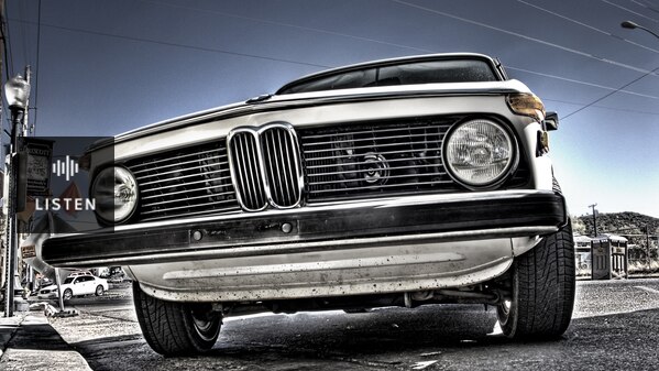 From a low angle, you look up at an old, white BMW sedan, with the focal point on its grille. Has Audio.