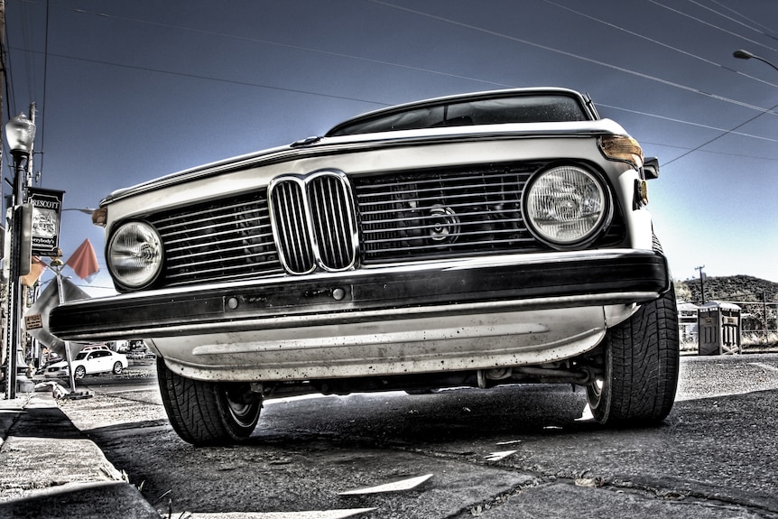 From a low angle, you look up at an old, white BMW sedan, with the focal point on its grille.