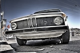 From a low angle, you look up at an old, white BMW sedan, with the focal point on its grille.