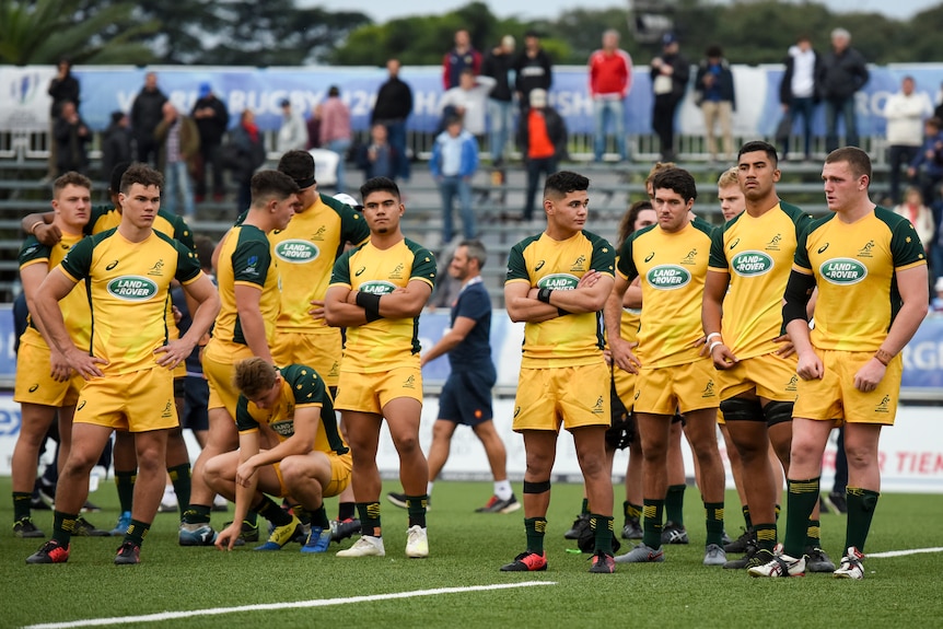 Rugby union players wearing yellow stand around looking sad after a game