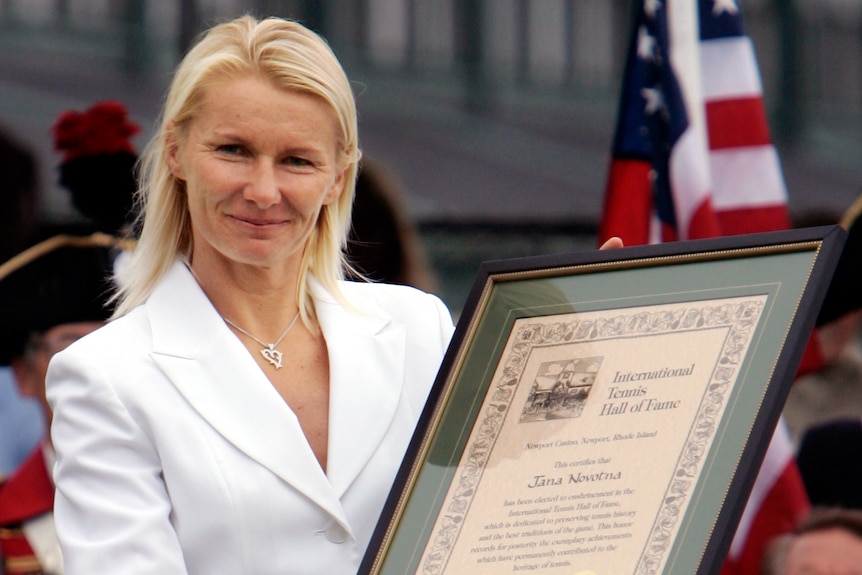 Jana Novotna wears a white suit and holds up her certificate after being inducted into the Tennis Hall of Fame.