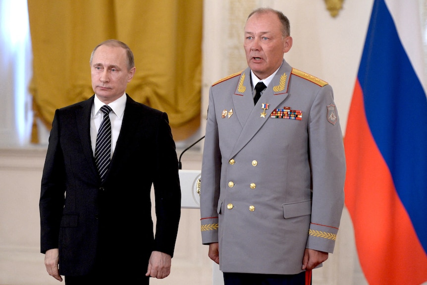 Two men stand for pictures in front of Russian flag.