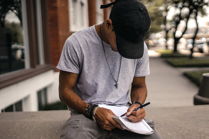Man has head down writing a note on paper