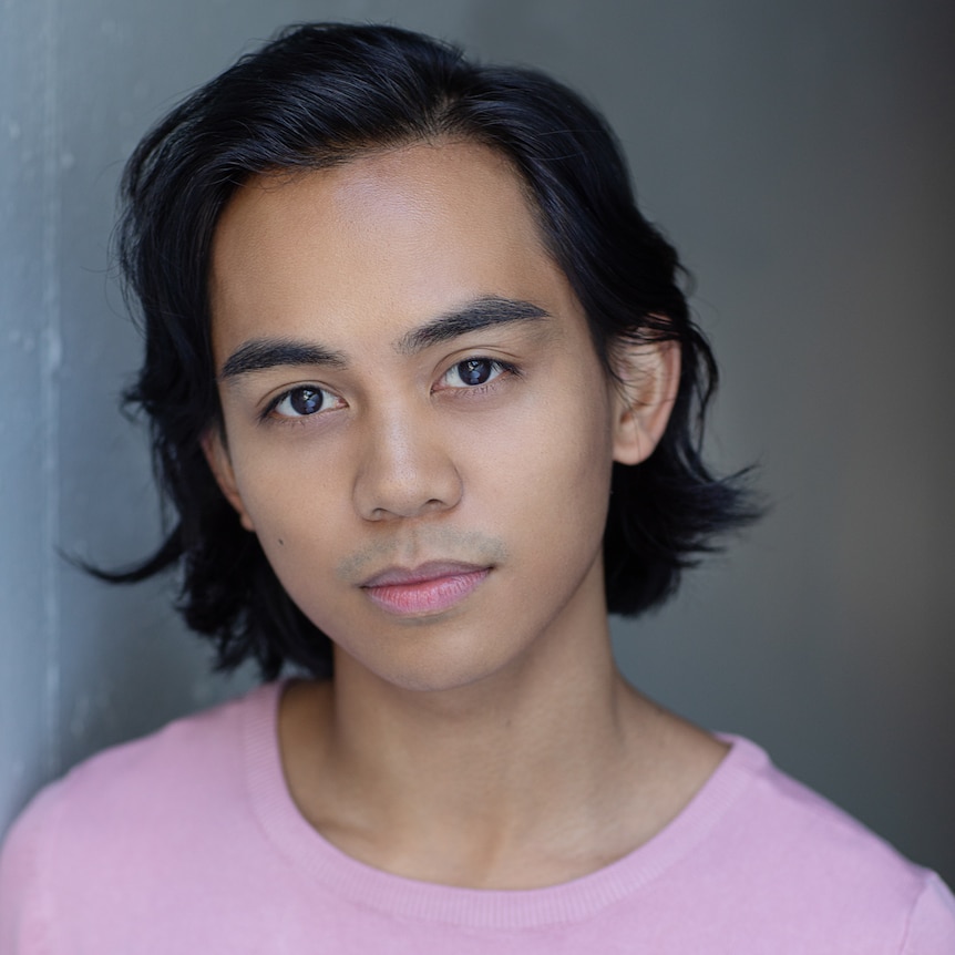 Young man with chin-length black hair, wearing long-sleeved light pink top.