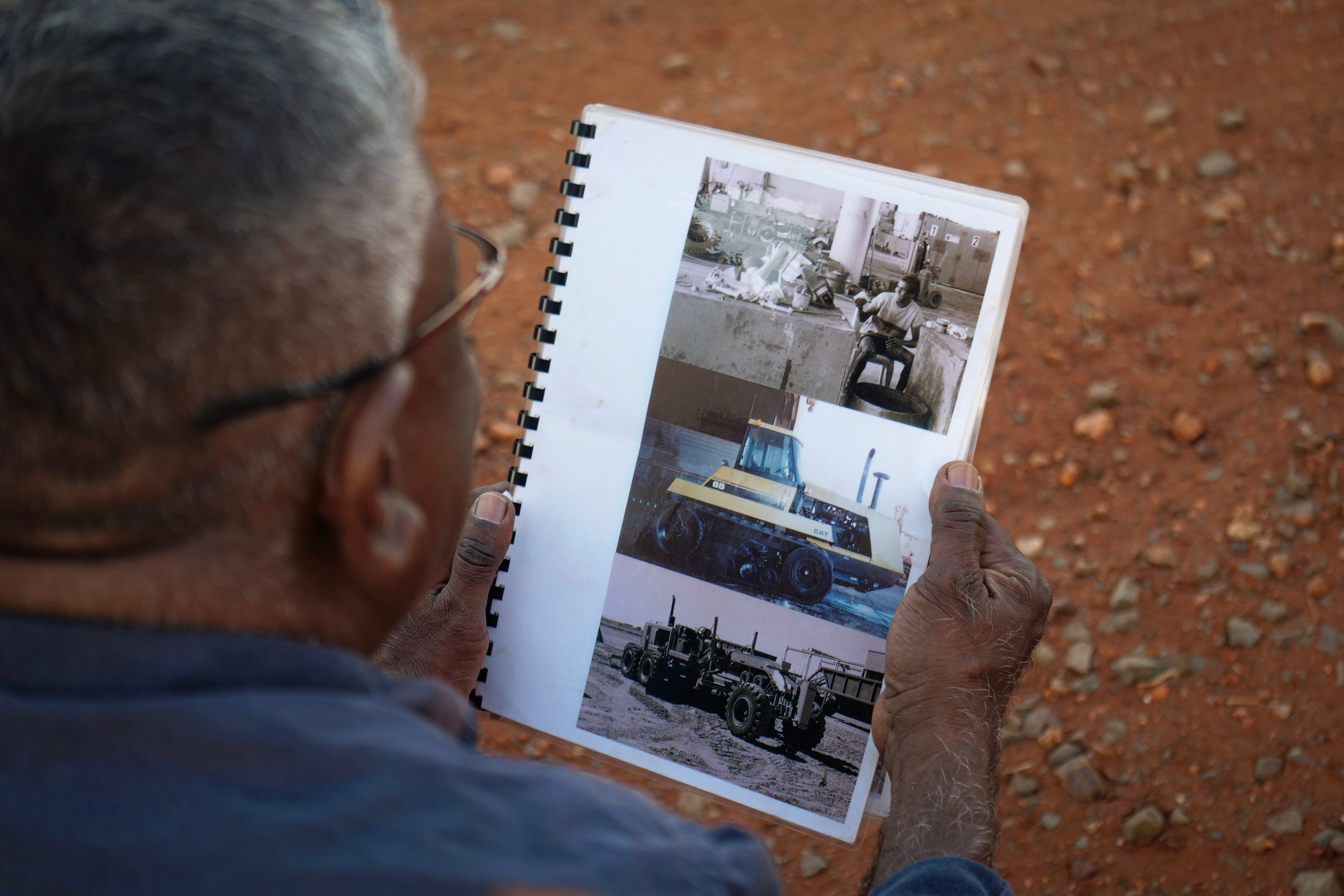 Un aborigen de mediana edad mira copias impresas de fotografías antiguas, incluida una versión más joven de sí mismo.