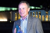 David Morrison stands in front of Parliament House, Canberra, at night with his Australian of the Year award.