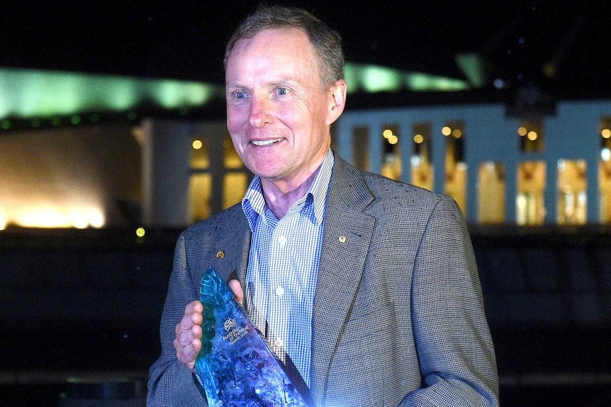 David Morrison stands in front of Parliament House, Canberra, at night with his Australian of the Year award.