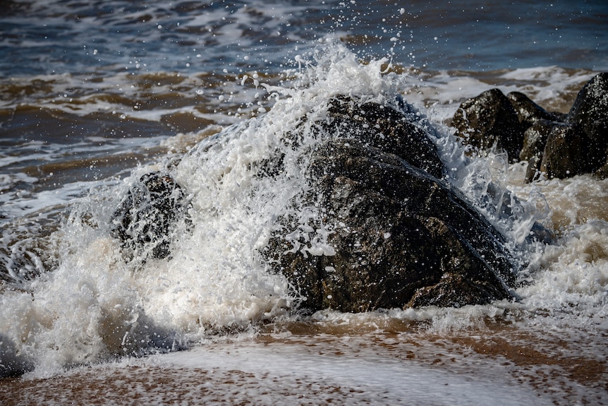 Water splashes over rocks on a beach.