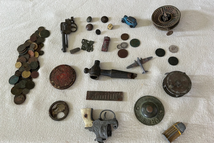 Old coins, parts of pistols, and toys are seen collected on a table.