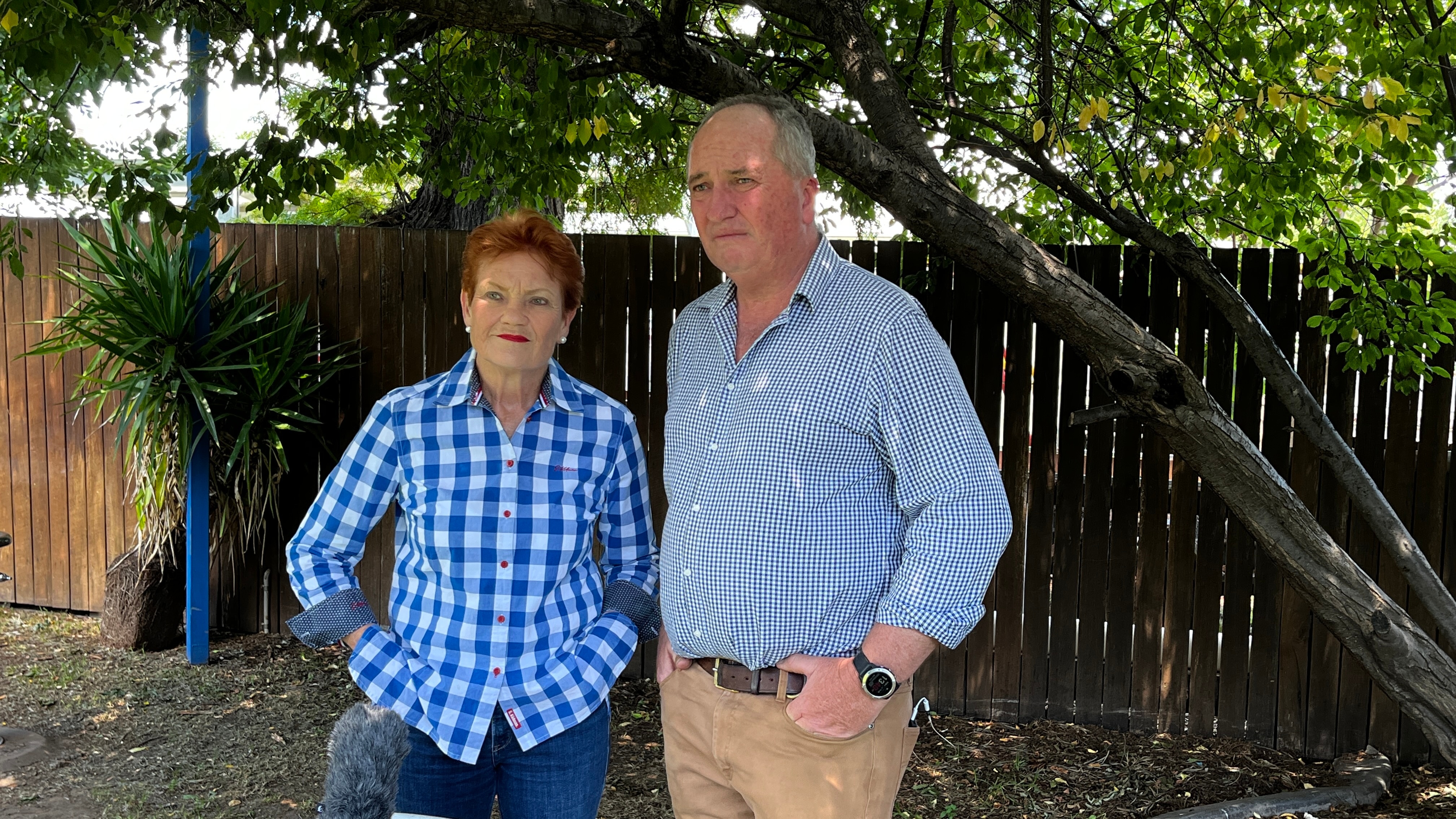 Um homem e uma mulher vestindo camisas de botão, em um ambiente ao ar livre. 